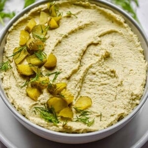 A bowl with the dip is in the center of the frame with herbs around it.