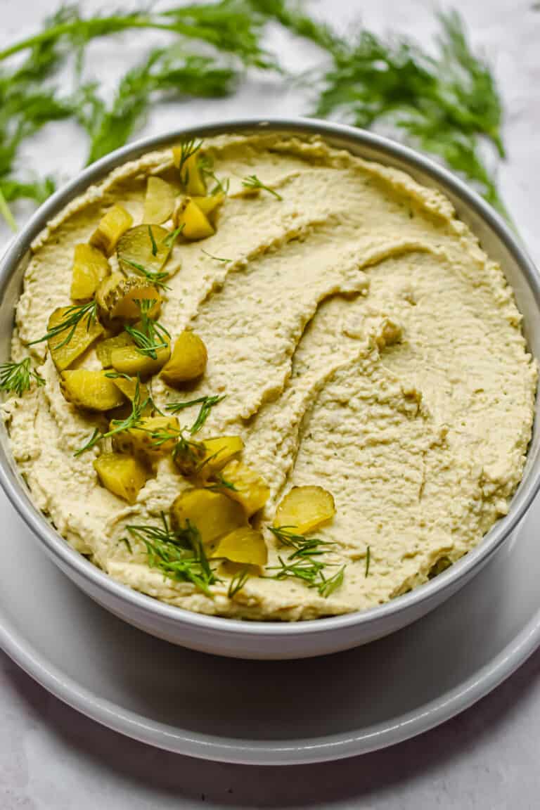 A bowl with the dip is in the center of the frame with herbs around it.