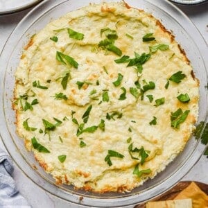 The dip is in a clear baking dish surrounded by pita chips and parsley.