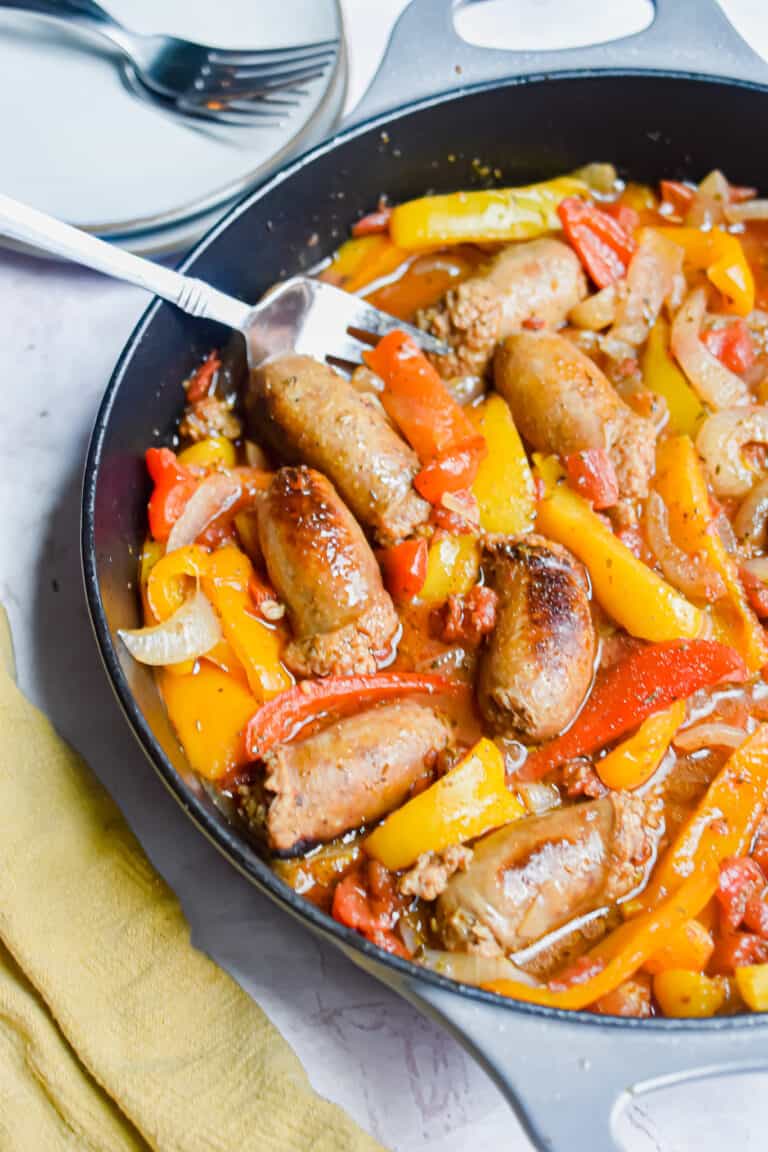 A fork is in the pan with the one pot sausage and peppers and a yellow napkin on the corner of the pan.