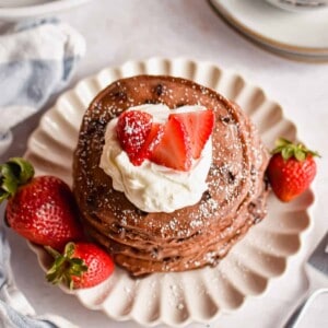 An overhead shot of a stack of chocolate pancakes with pancake mix topped with strawberries and whipped cream.