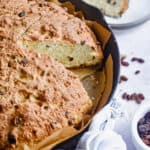 A piece of sourdough irish soda bread is on a plate next to the cast iron skillet.