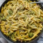The one pot sausage broccoli pasta is surrounded by black pepper and a towel.