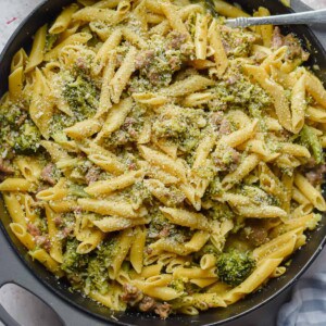 The one pot sausage broccoli pasta is surrounded by black pepper and a towel.
