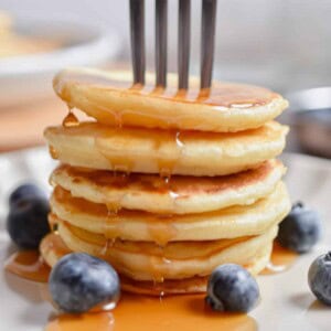 A fork is in a stack of silver dollar pancakes with maple syrup.