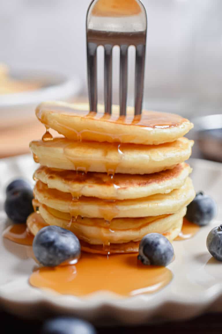 A fork is in a stack of silver dollar pancakes with maple syrup.