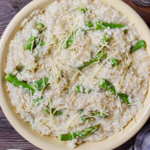 A bowl of Instant Pot Asparagus Risotto is in a bowl surrounded by cheese and a cloth.
