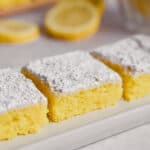 Three 2 ingredient lemon bars are on a rectangular plate with lemons in the background.