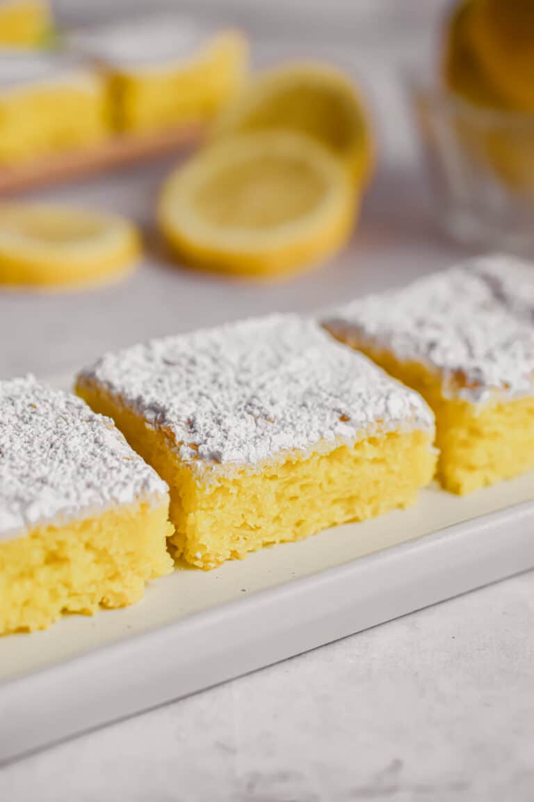 Three 2 ingredient lemon bars are on a rectangular plate with lemons in the background.