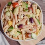 A bowl of Greek Pasta Salad with Penne Pasta is sitting on a cutting board.