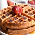 Maple syrup is being poured on a stack of strawberry waffles.