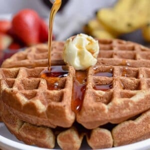 Maple syrup is being poured onto the whole wheat waffles.
