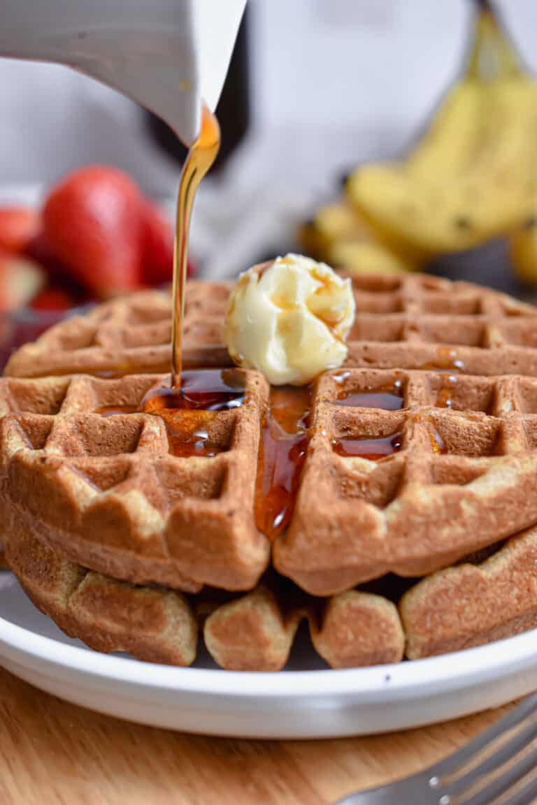 Maple syrup is being poured onto the whole wheat waffles.