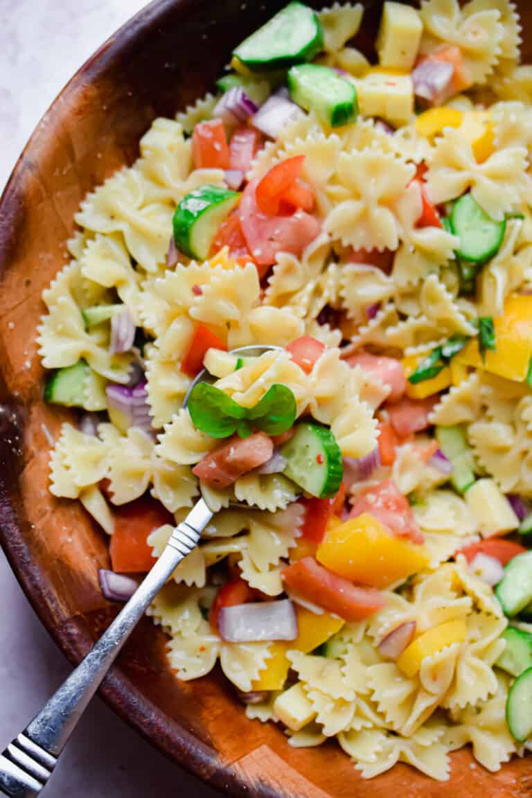 A spoon is holding some of the bowtie pasta salad with Italian dressing