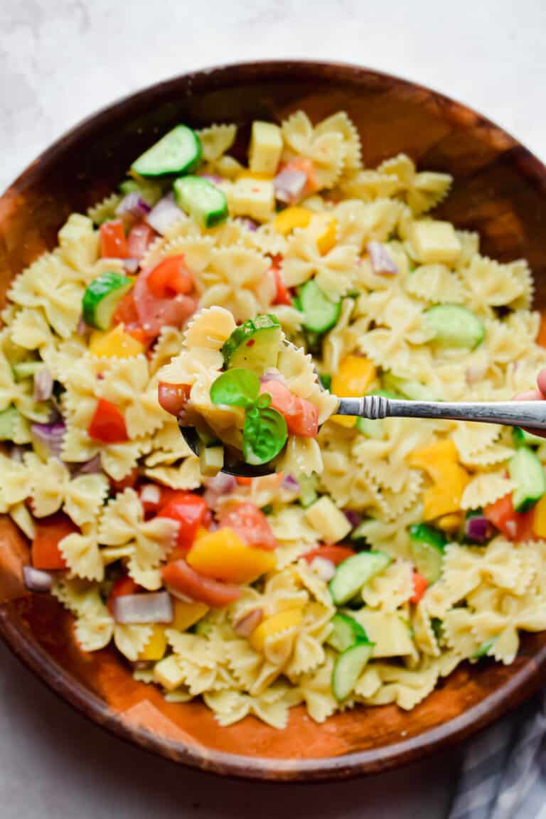 A spoon is holding a portion of the Bowtie Pasta Salad with italian Dressing over the large bowl.