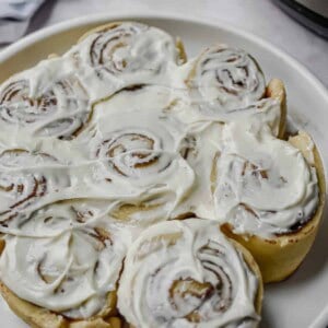 A plate of Instant Pot Cinnamon Rolls is in front of the Instant Pot.