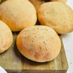 One sourdough hamburger bun has seeds on a cutting board.