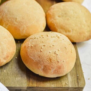 One sourdough hamburger bun has seeds on a cutting board.