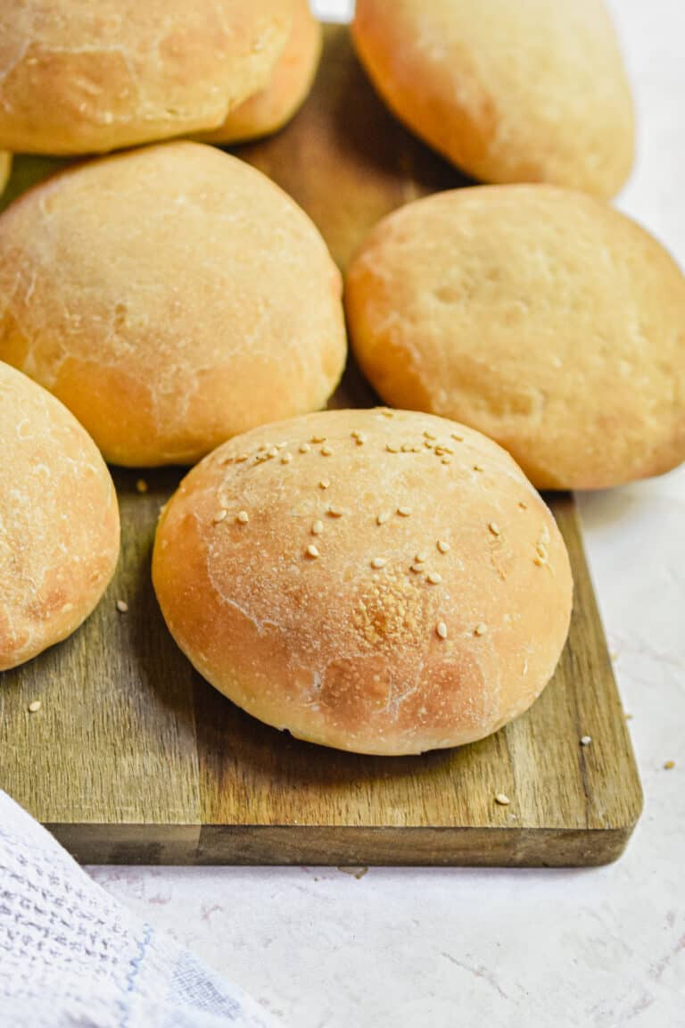 One sourdough hamburger bun has seeds on a cutting board.