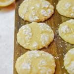 The 3 ingredient lemon cookies are laid out on a cutting board with a cut lemon in the background.