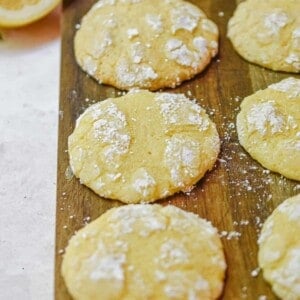 The 3 ingredient lemon cookies are laid out on a cutting board with a cut lemon in the background.