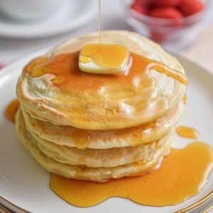 Maple syrup is being drizzled over a stack of almond milk pancakes.