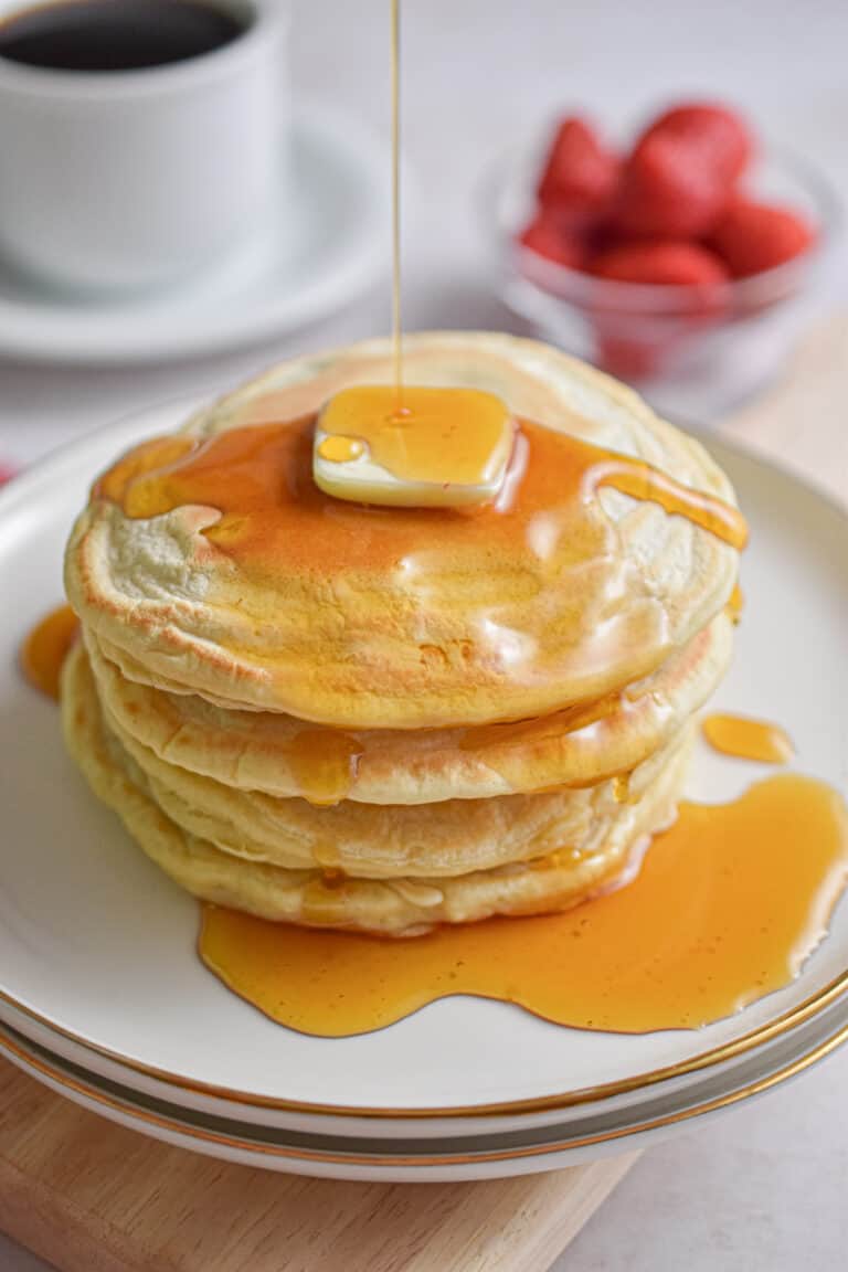 Maple syrup is being drizzled over a stack of almond milk pancakes.