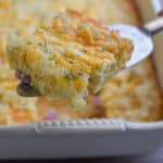 A pie cutter is holding a piece of the bisquick breakfast casserole over the casserole dish.