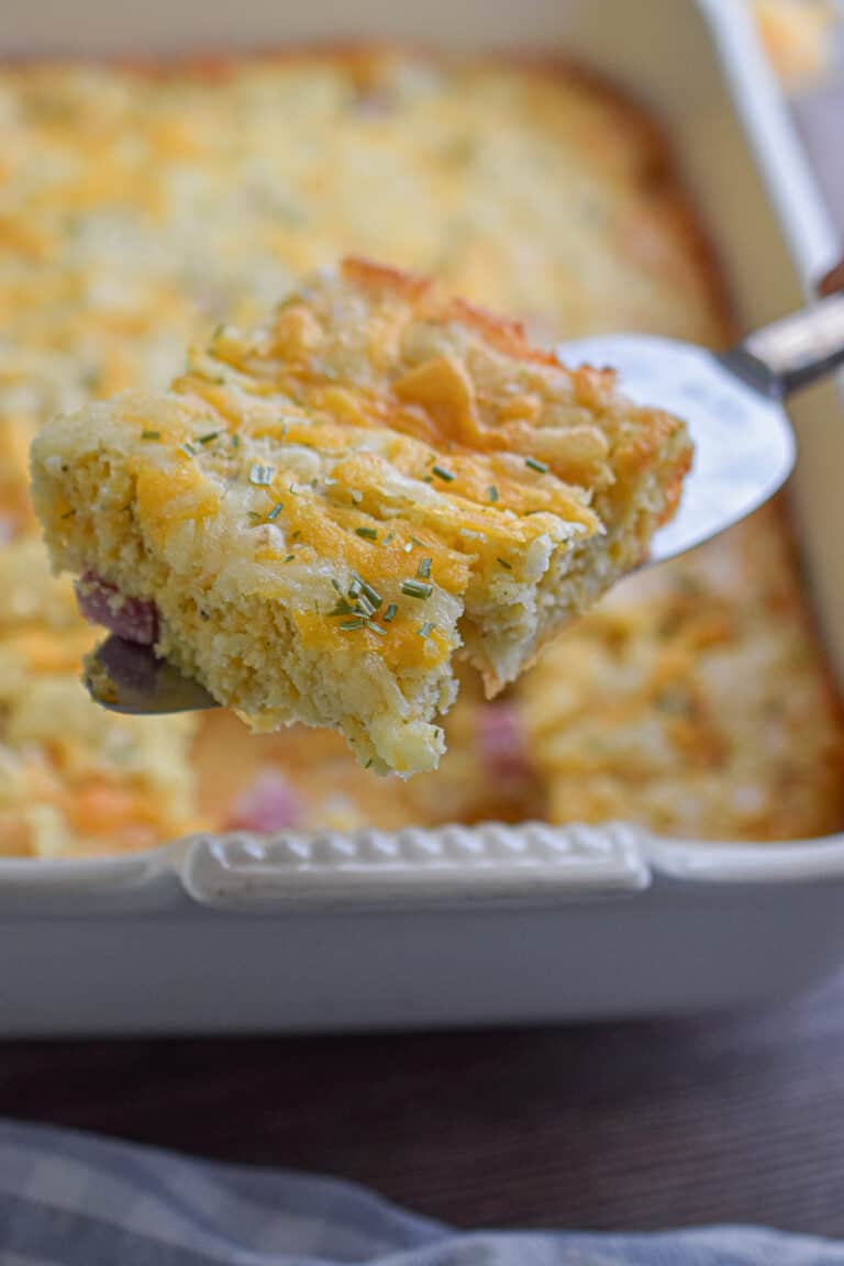 A pie cutter is holding a piece of the bisquick breakfast casserole over the casserole dish.