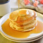 Maple syrup is being poured onto a stack of pancakes without milk.