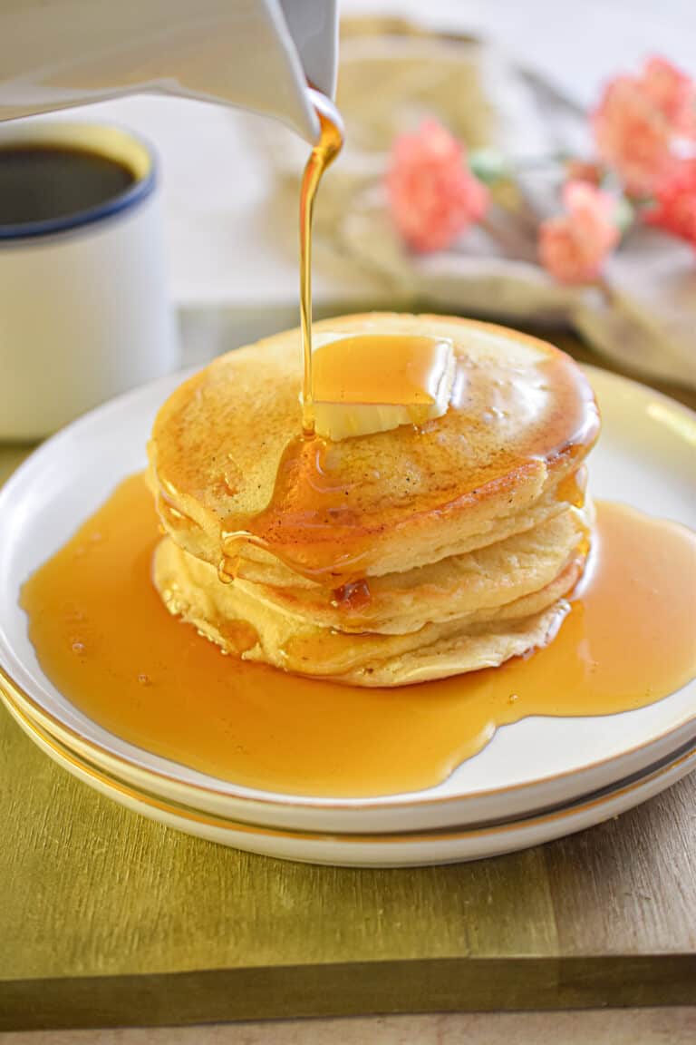 Maple syrup is being poured onto a stack of pancakes without milk.