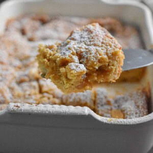 A pie cutter is holding a piece of the apple pie coffee cake.
