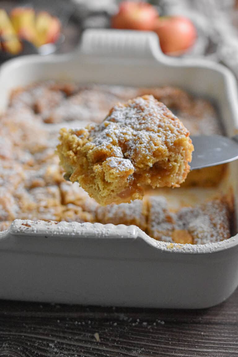 A pie cutter is holding a piece of the apple pie coffee cake.