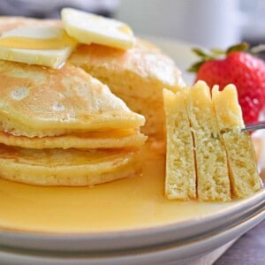 The pancakes recipe for one has been made and stacked with a fork cutting a piece of the stack and holding it.