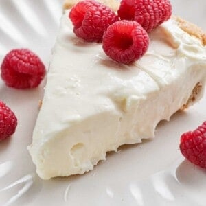 Raspberries top the 3-ingredient no bake cheesecake on a fluted plate.