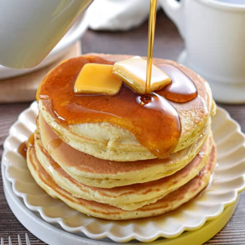 Maple syrup is being poured on a stack of Bisquick pancakes.