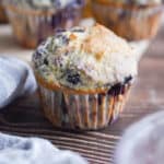 A blueberry muffin with pancake mix is surrounded by a blue napkin and more muffins in the background.