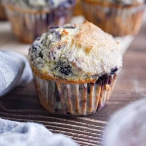 A blueberry muffin with pancake mix is surrounded by a blue napkin and more muffins in the background.
