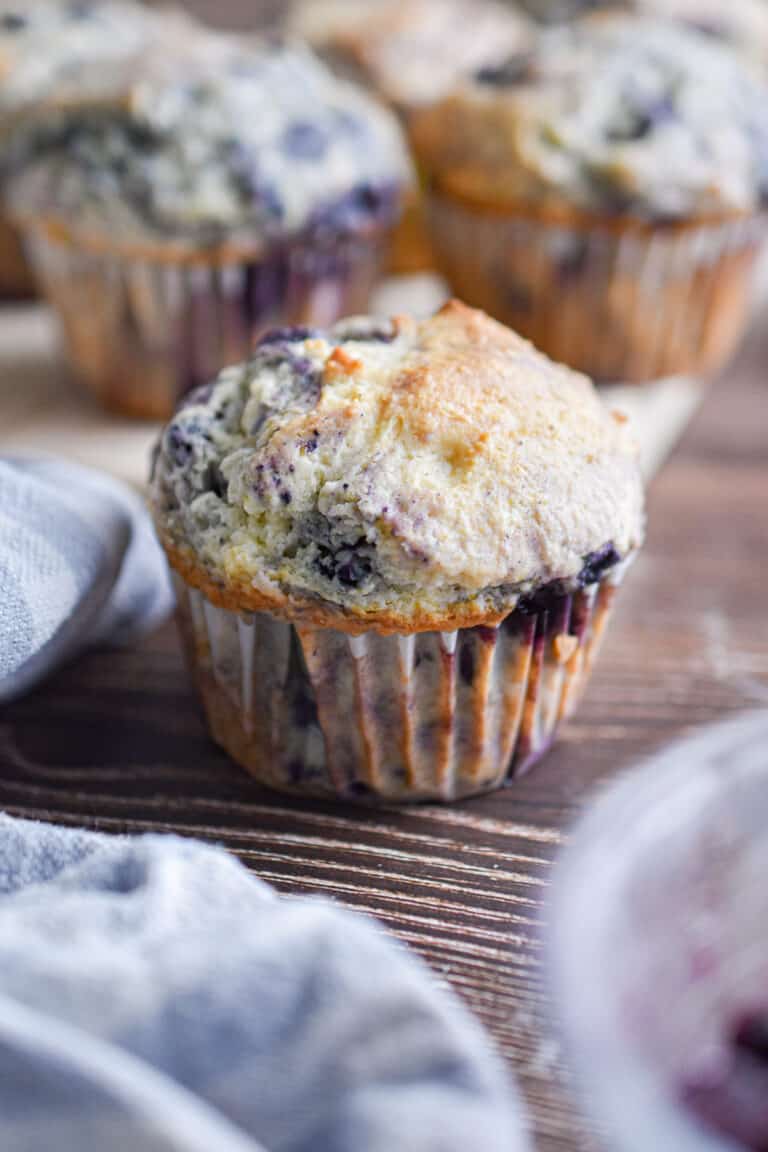 A blueberry muffin with pancake mix is surrounded by a blue napkin and more muffins in the background.