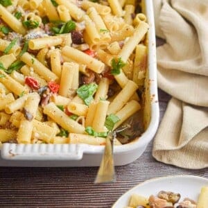 A napkin is behind the baking dish with the Greek Pasta Bake in it and a portion is on a plate in front of the baking dish.