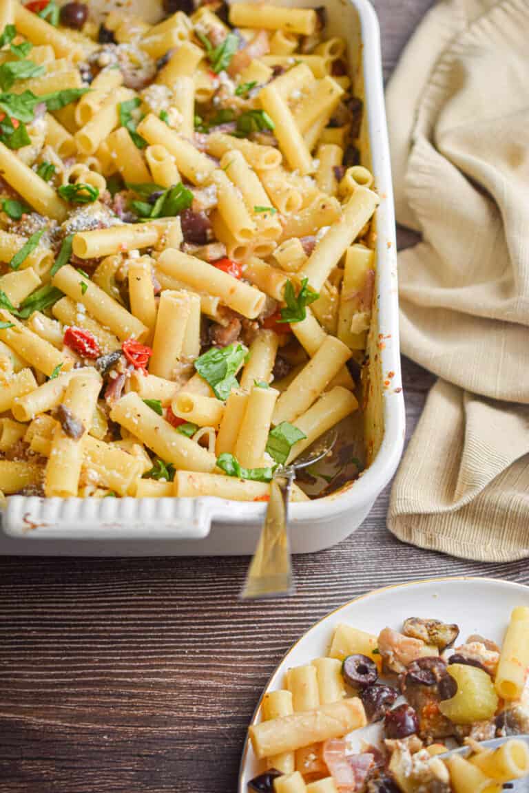 A napkin is behind the baking dish with the Greek Pasta Bake in it and a portion is on a plate in front of the baking dish.