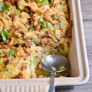 The Italian sausage stuffing is in a baking dish and a spoon is in the baking dish.