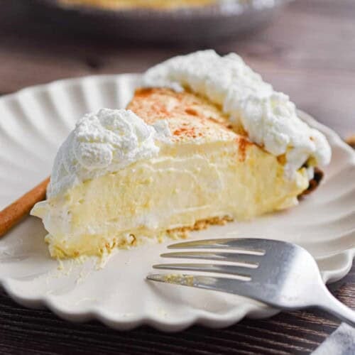 A slice of the no-bake eggnog pie is on a plate with a fork and a cinnamon stick.