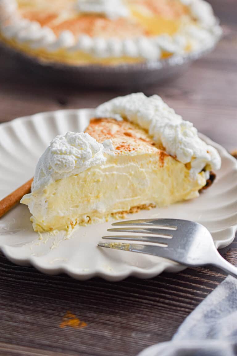 A slice of the no-bake eggnog pie is on a plate with a fork and a cinnamon stick.