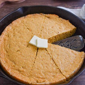 The sweet potato cornbread is in an iron skillet with two tabs of butter on it.