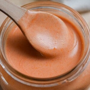 A spoon is lifting the creamy buffalo sauce out of the mason jar on a cutting board.
