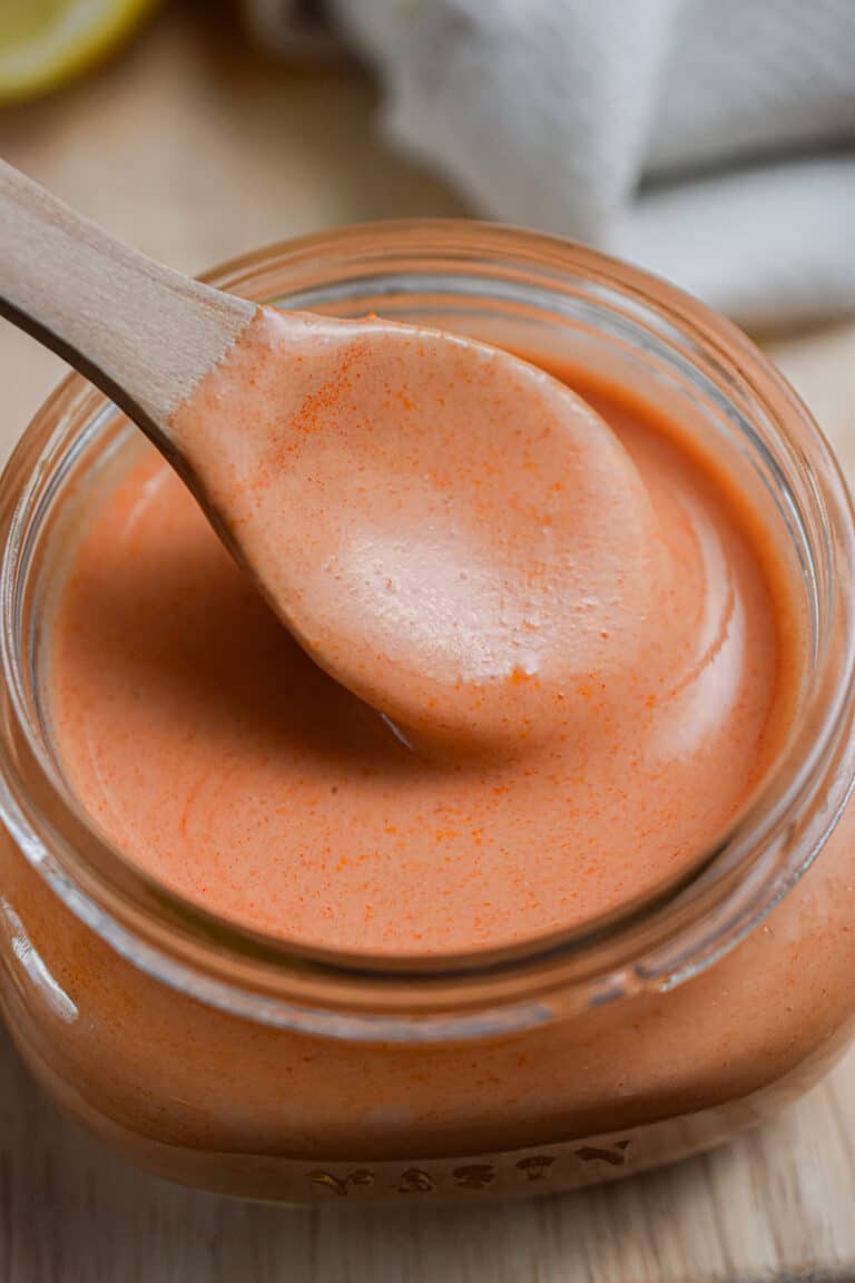 A spoon is lifting the creamy buffalo sauce out of the mason jar on a cutting board.