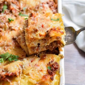 A piece of the meat lovers lasagna is being taken out of the baking dish.