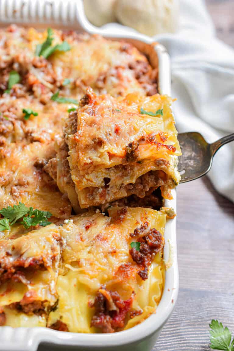 A piece of the meat lovers lasagna is being taken out of the baking dish.