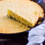 A piece of the cornbread with self rising flour is lifted out of the cast iron skillet.